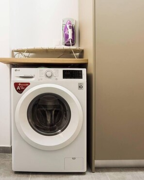 A front-loading washing machine with a control panel, a hanging rack, and a wall-mounted iron. - Comfort Zone Apartment in the heart of Athens (Athina)