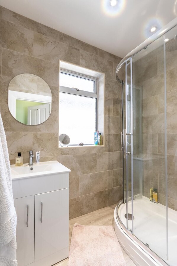 A bathroom with a glass shower enclosure, a sink with a mirror, and a window above the sink.
