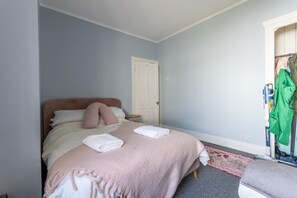 A bedroom with a single bed, a bedside table, a door, and a closet with hanging clothes.