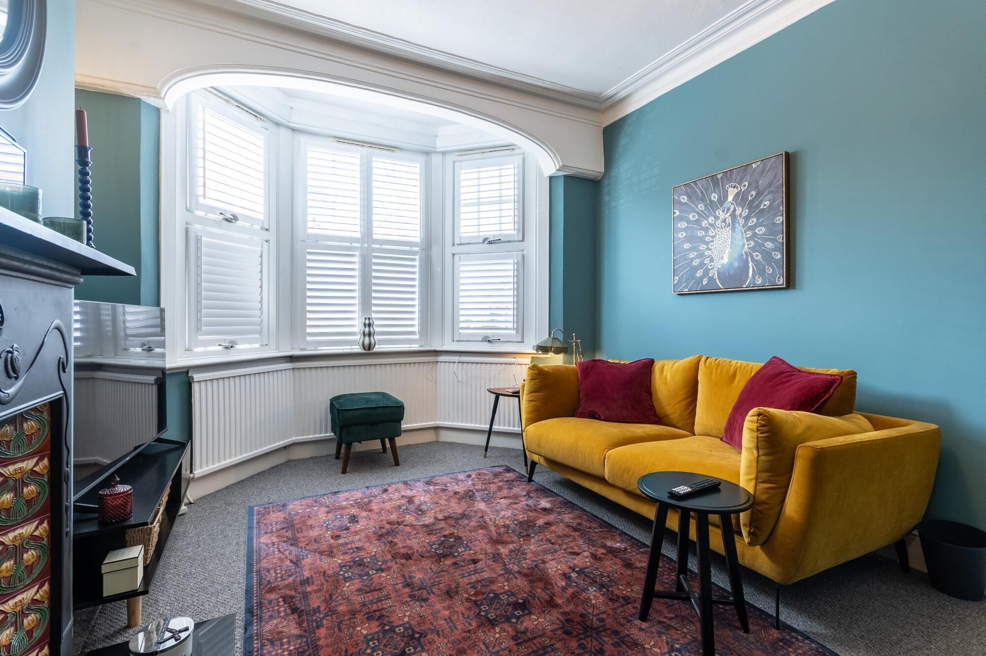 Une pièce avec une baie vitrée, un canapé jaune, un tapis à motifs et un tableau accroché au mur.