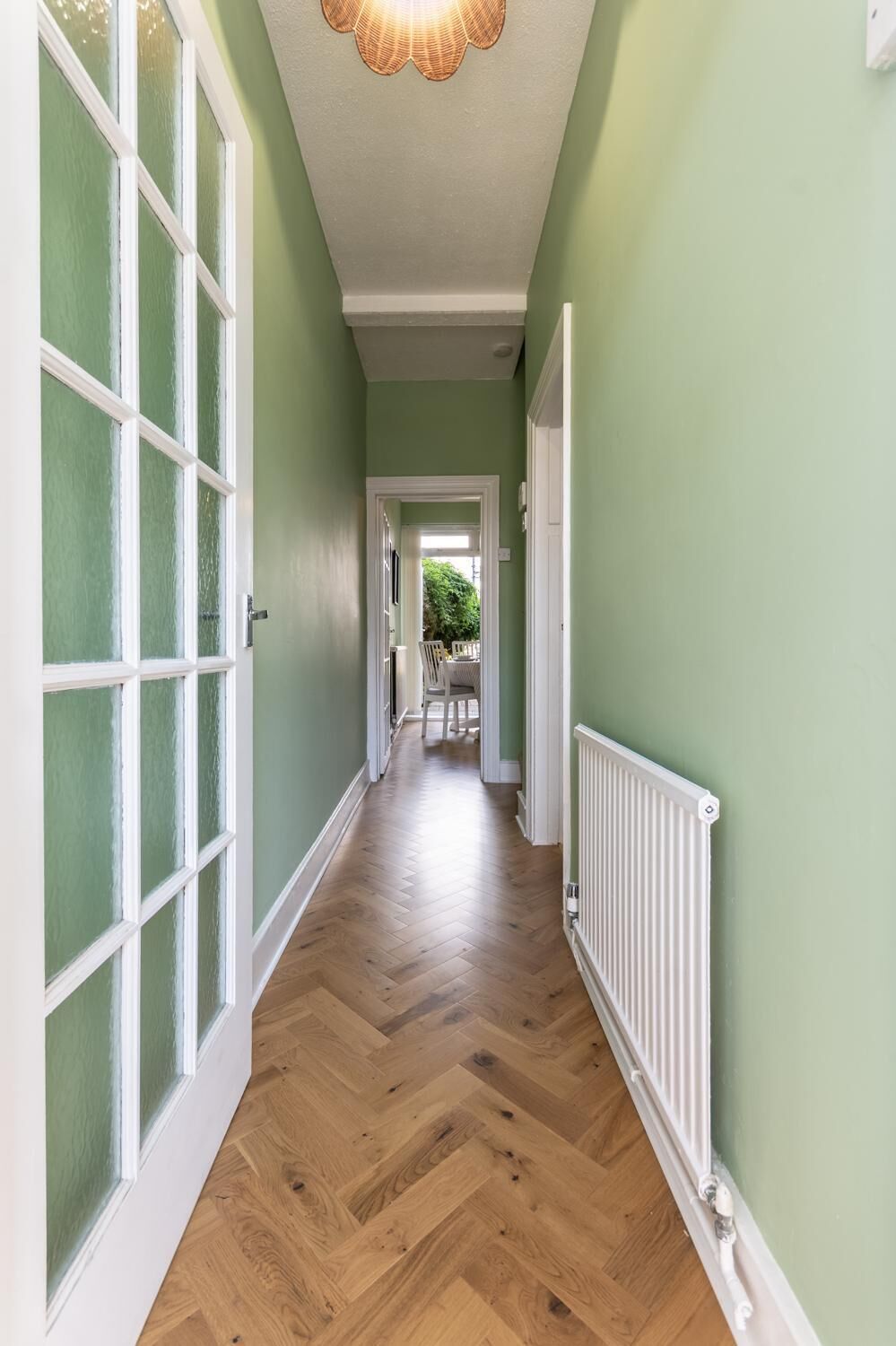 A hallway with a herringbone floor, a radiator, and a door with frosted glass panels.