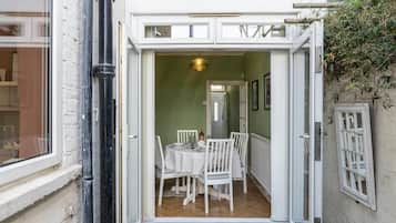 Une porte ouverte donne sur un coin repas où une table est dressée pour deux personnes, avec un luminaire suspendu et une vue sur la pièce adjacente.