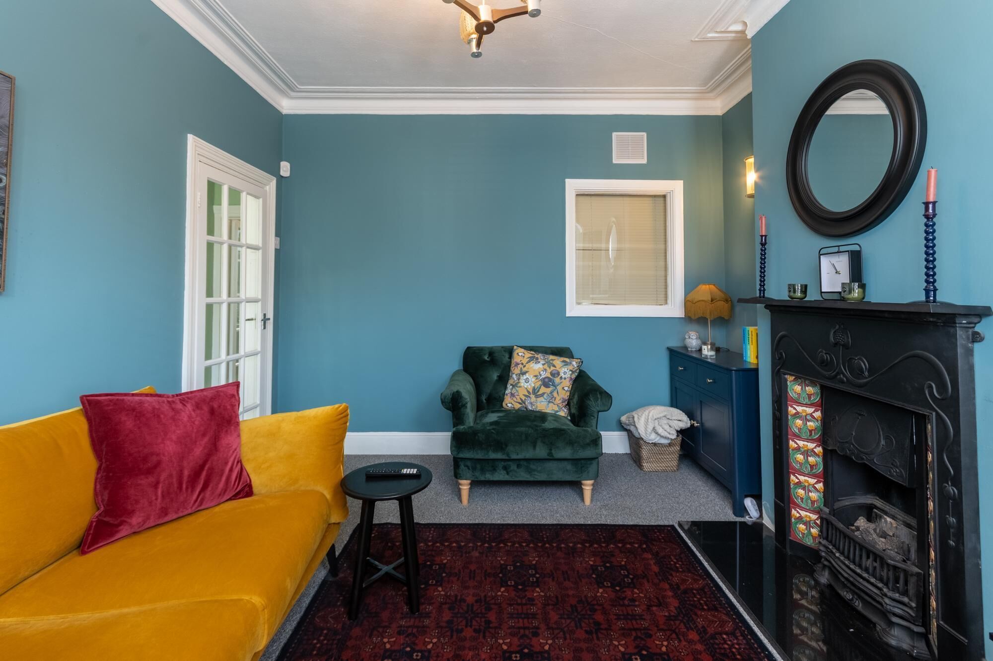 A living room with a yellow sofa, a green armchair, a fireplace, and a blue wall.