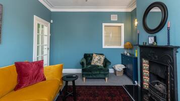 A living room with a yellow sofa, a green armchair, a fireplace, and a blue wall.