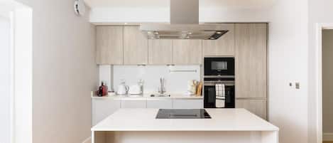 A modern kitchen with a central island, built-in appliances, and light wood cabinetry.