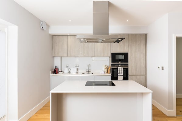 Une cuisine moderne dotée d’un îlot central, d’appareils électroménagers intégrés et de meubles de cuisine en bois clair.