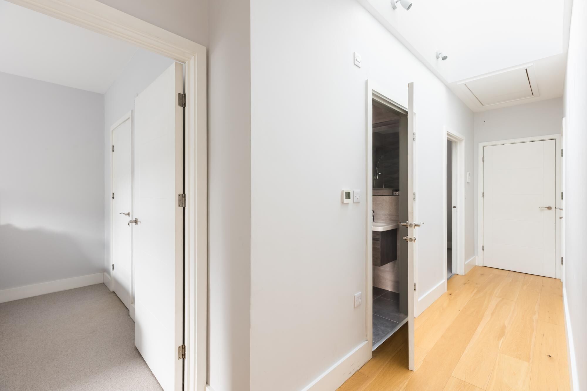 A hallway with white walls and wooden flooring, leading to a bathroom with a shower and a toilet.
