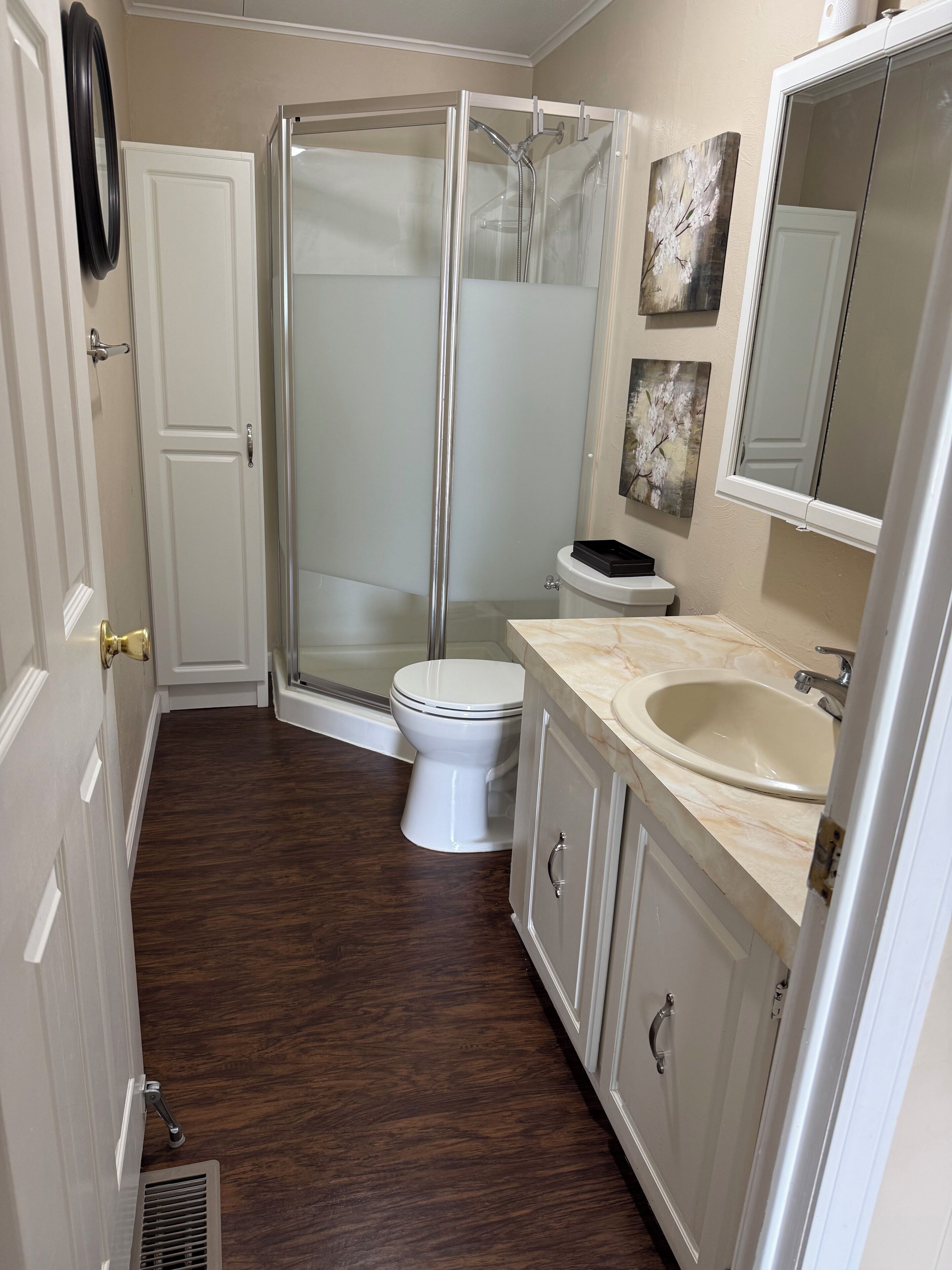 Un baño con ducha envuelta en vidrio, un inodoro, un lavabo y un armario.
