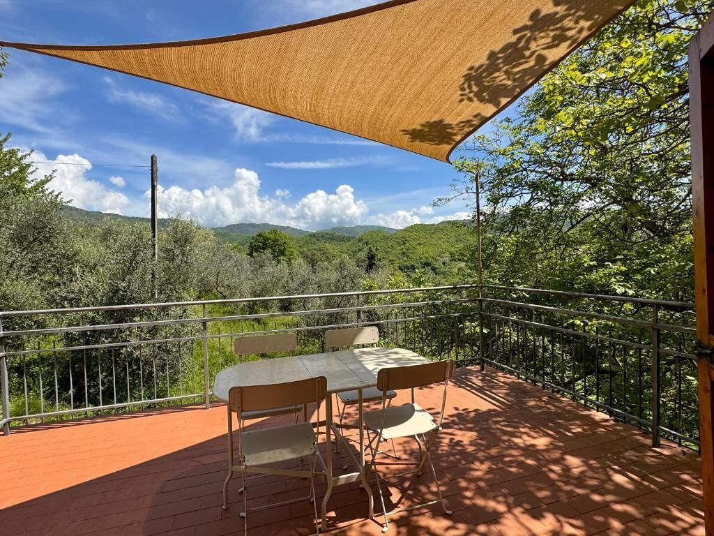 Eine Terrasse im Freien mit Tisch und Stühlen, umgeben von einem Metallgeländer, mit Blick auf eine gebirgige Landschaft.
