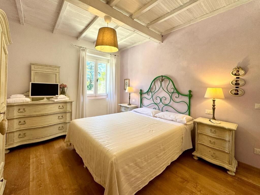 A bedroom with a bed, bedside tables, a dresser, a mirror, and a window with curtains.