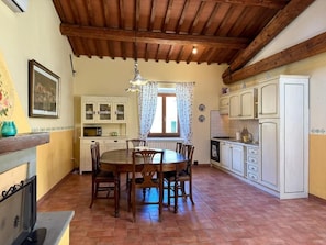 Un comedor con mesa y sillas de madera, una cocina con armarios blancos y una ventana con cortinas estampadas.