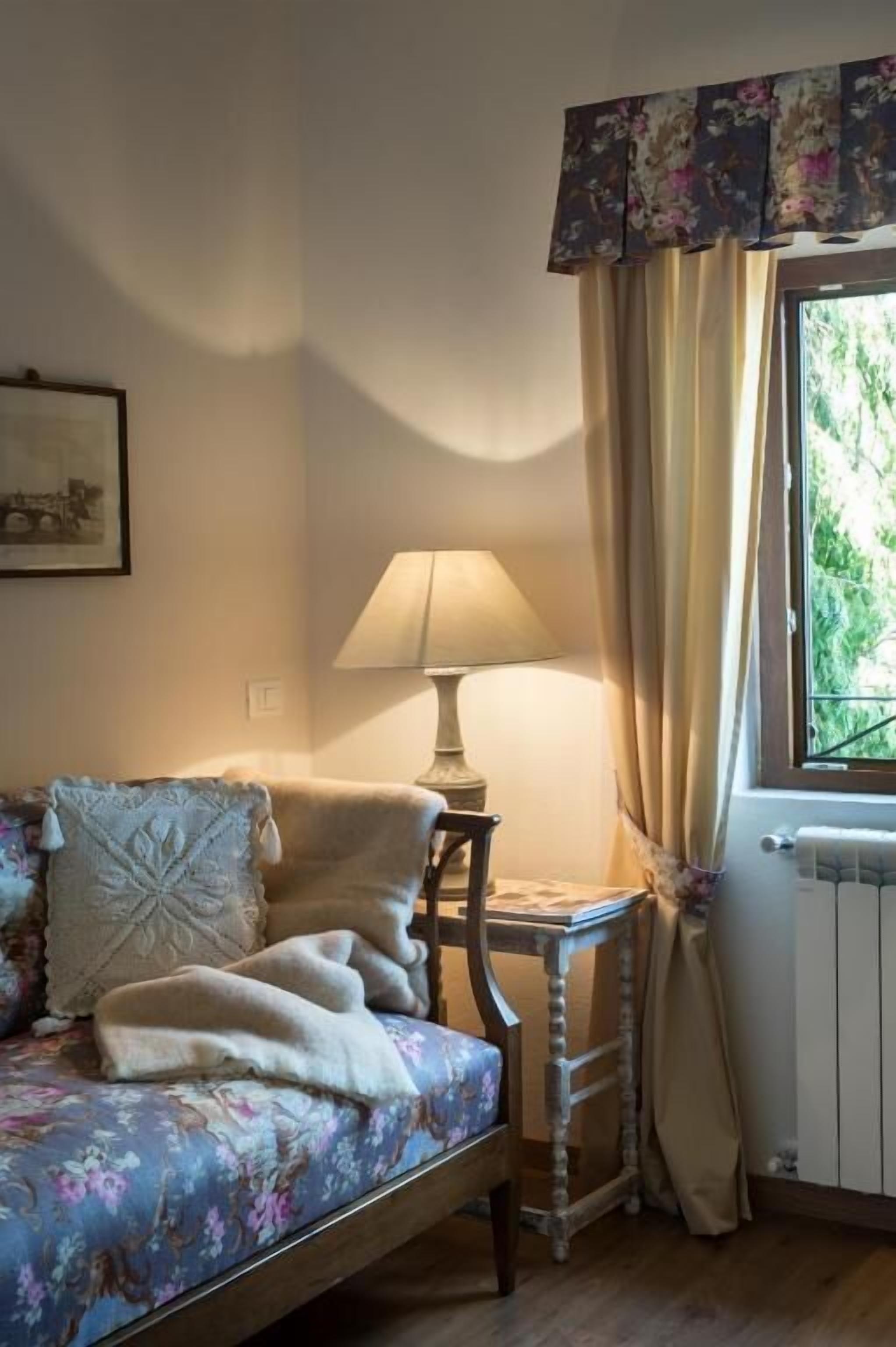 A room with a bed, a table, a lamp, and a window with curtains.