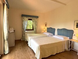 Un dormitorio con dos camas, una ventana con cortinas, una mesita de noche con lámpara y un armario pequeño.