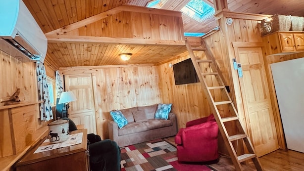 En mysig stuga med en inredd loftvåning, en soffa, ett skrivbord och en stege som leder upp till en sovplats på loftet.