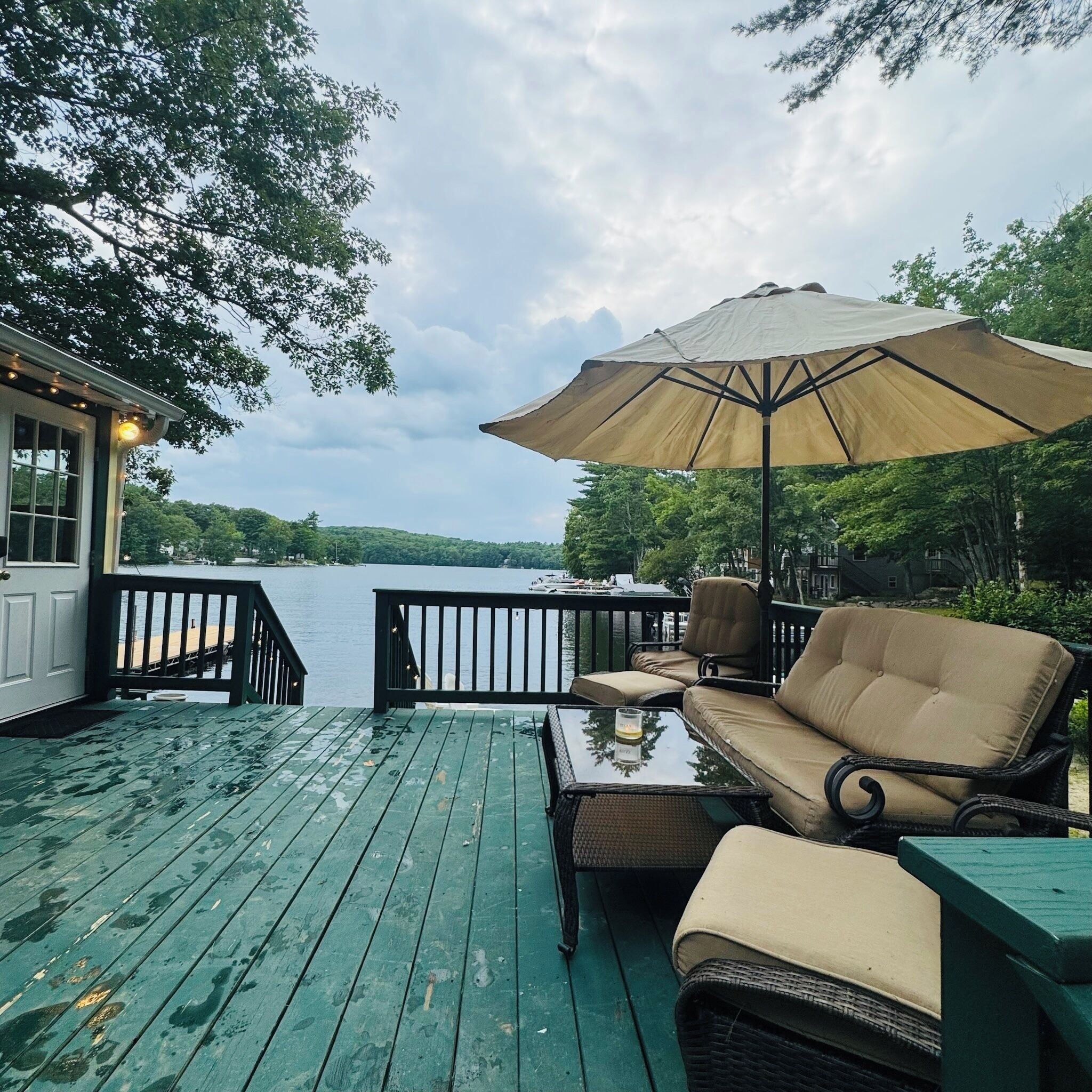 A deck with outdoor furniture, a table, and an umbrella overlooking a body of water.
