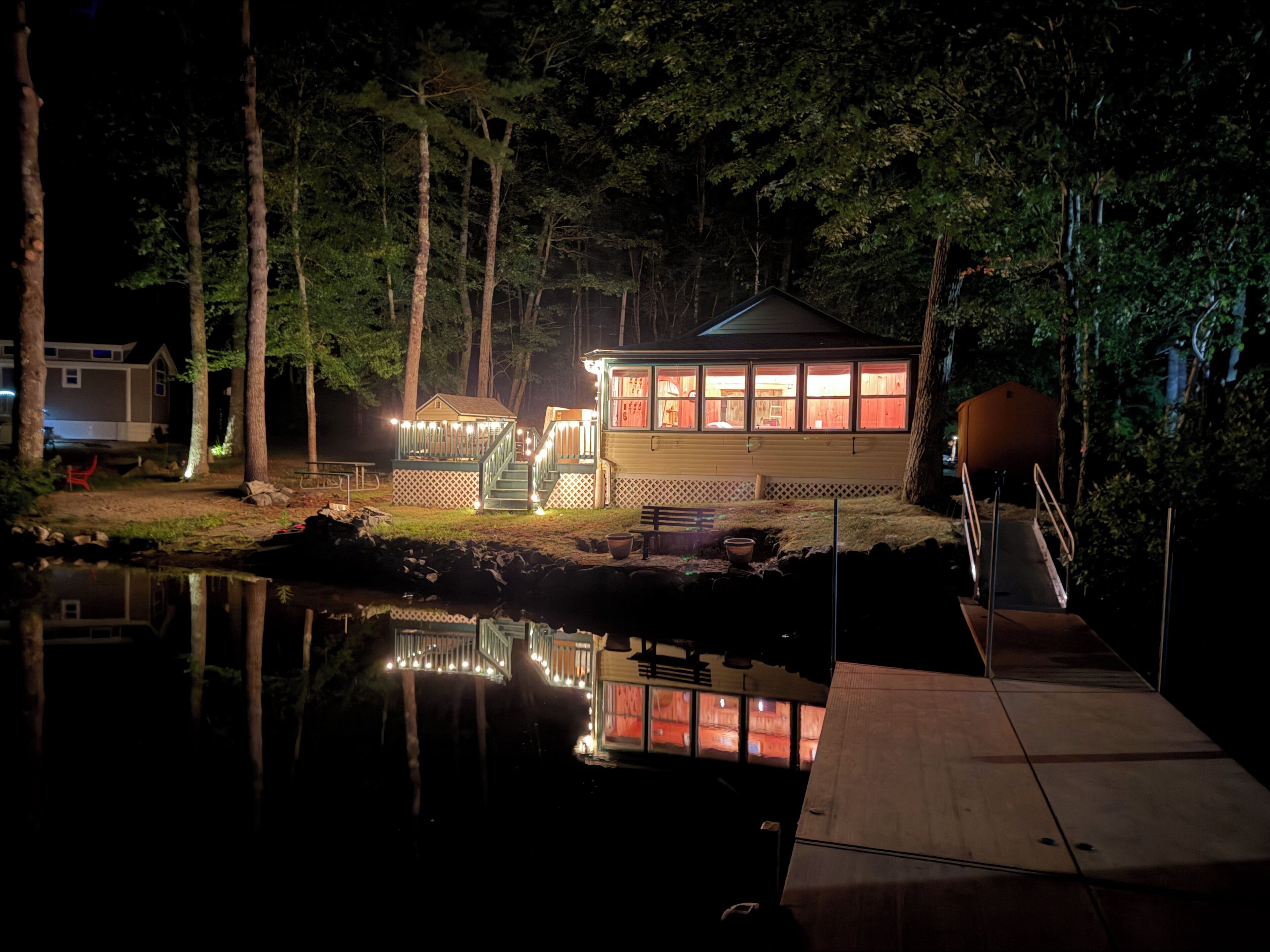 A cabin with a dock extending into a calm body of water, surrounded by trees.