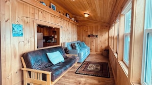 En inredning med träpanel, en soffa, ett matområde och en hall som leder till ett fönster.