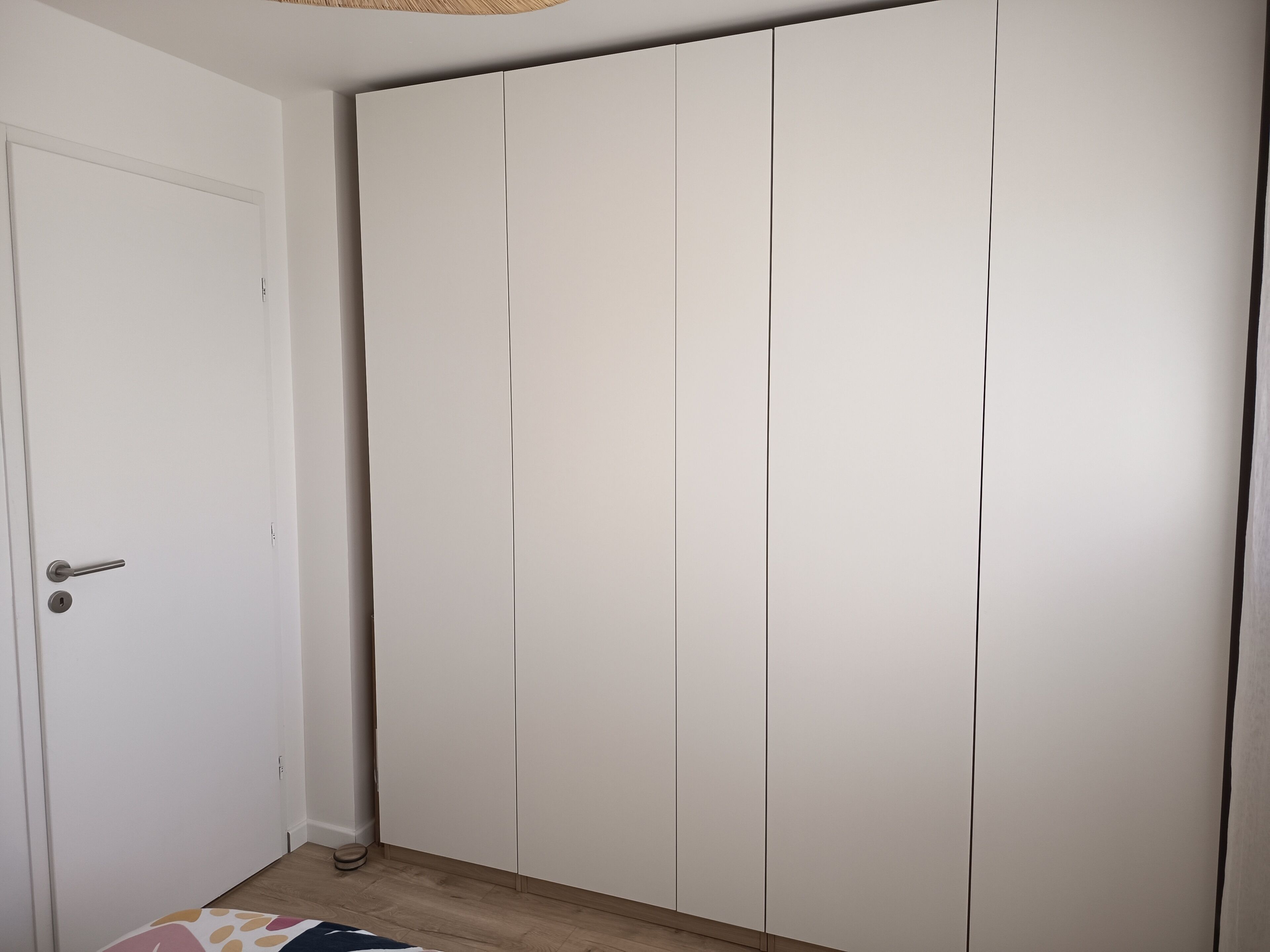 Een kamer met een witte garderobe, een deur met een handgreep, en een houten vloer.