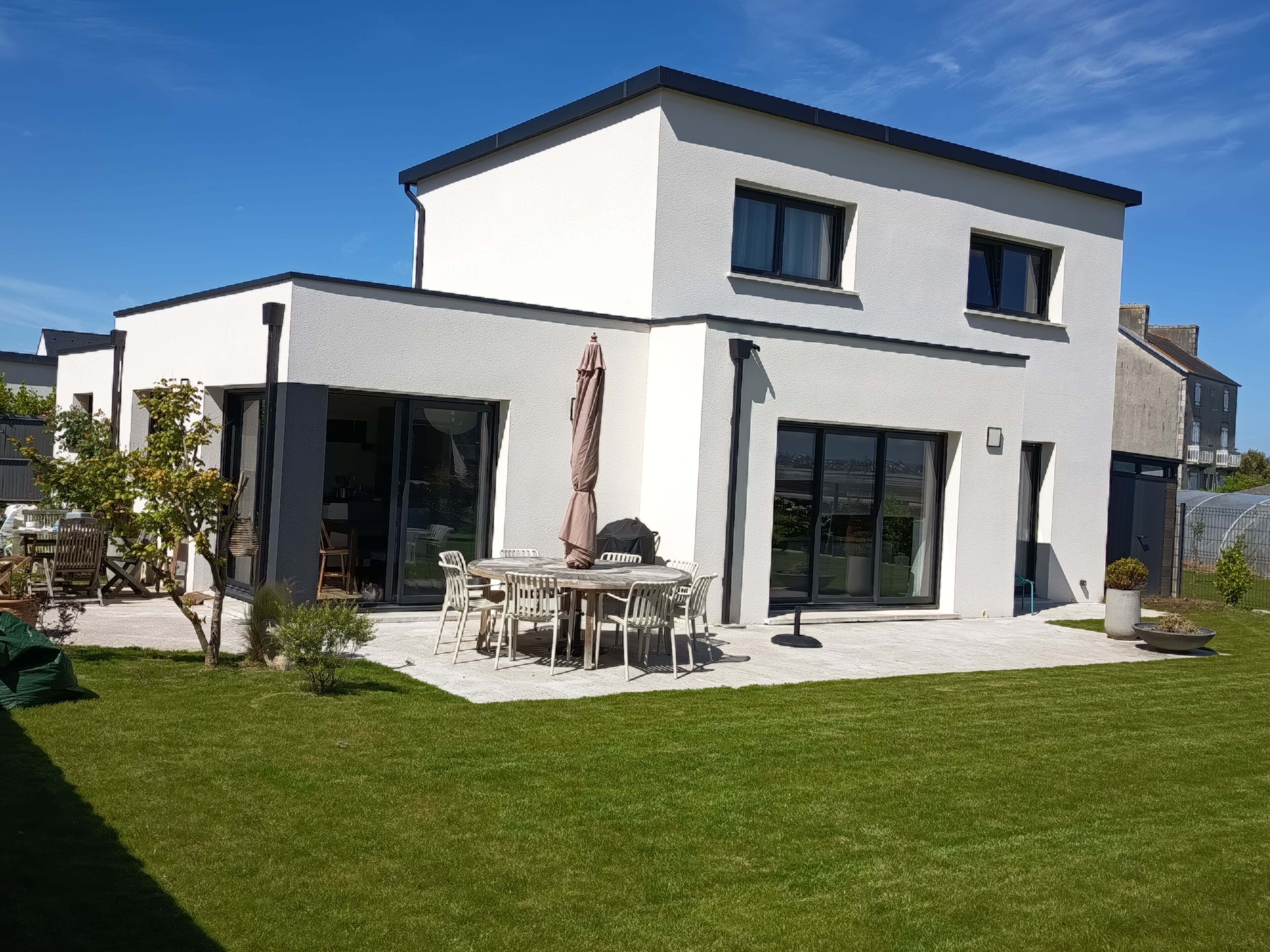 Een modern huis met twee verdiepingen, een patio, een eettafel en stoelen.