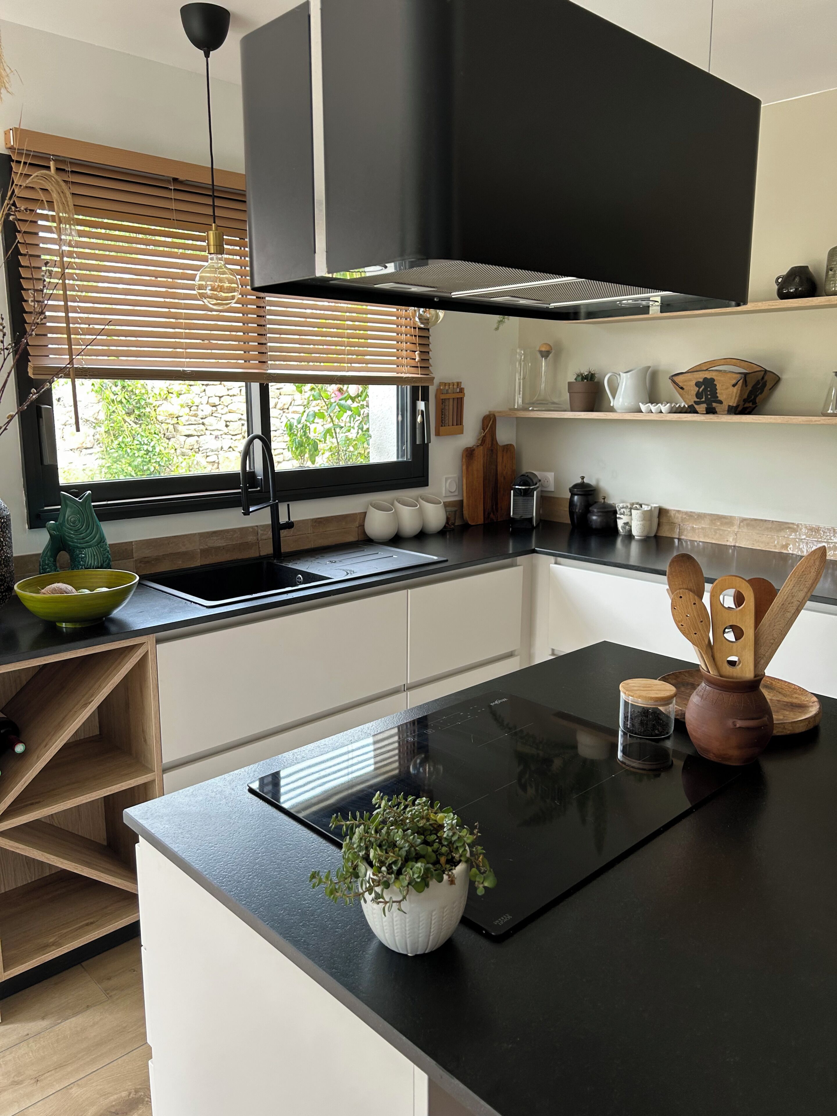 Una cocina moderna con encimera negra, horno empotrado y ventana con persianas.