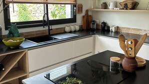 A modern kitchen with a black countertop, a built-in oven, and a window with blinds. - Sea view house 5 minutes walk from the beach and coastal paths. (Saint-Pol-de-Léon)