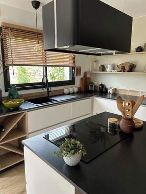 A modern kitchen with a black countertop, a built-in oven, and a window with blinds. - Sea view house 5 minutes walk from the beach and coastal paths. (Saint-Pol-de-Léon)