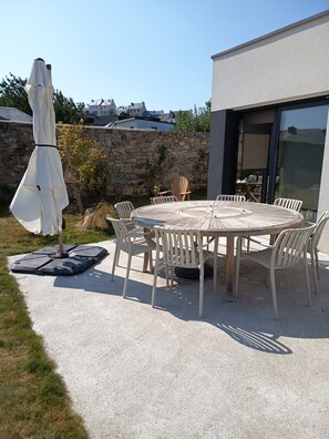 An outdoor patio with a round table and chairs, a white umbrella, and a stone wall. - House with ocean views, a 5-minute walk from the beach and coastal trails. (Saint-Pol-de-Léon)