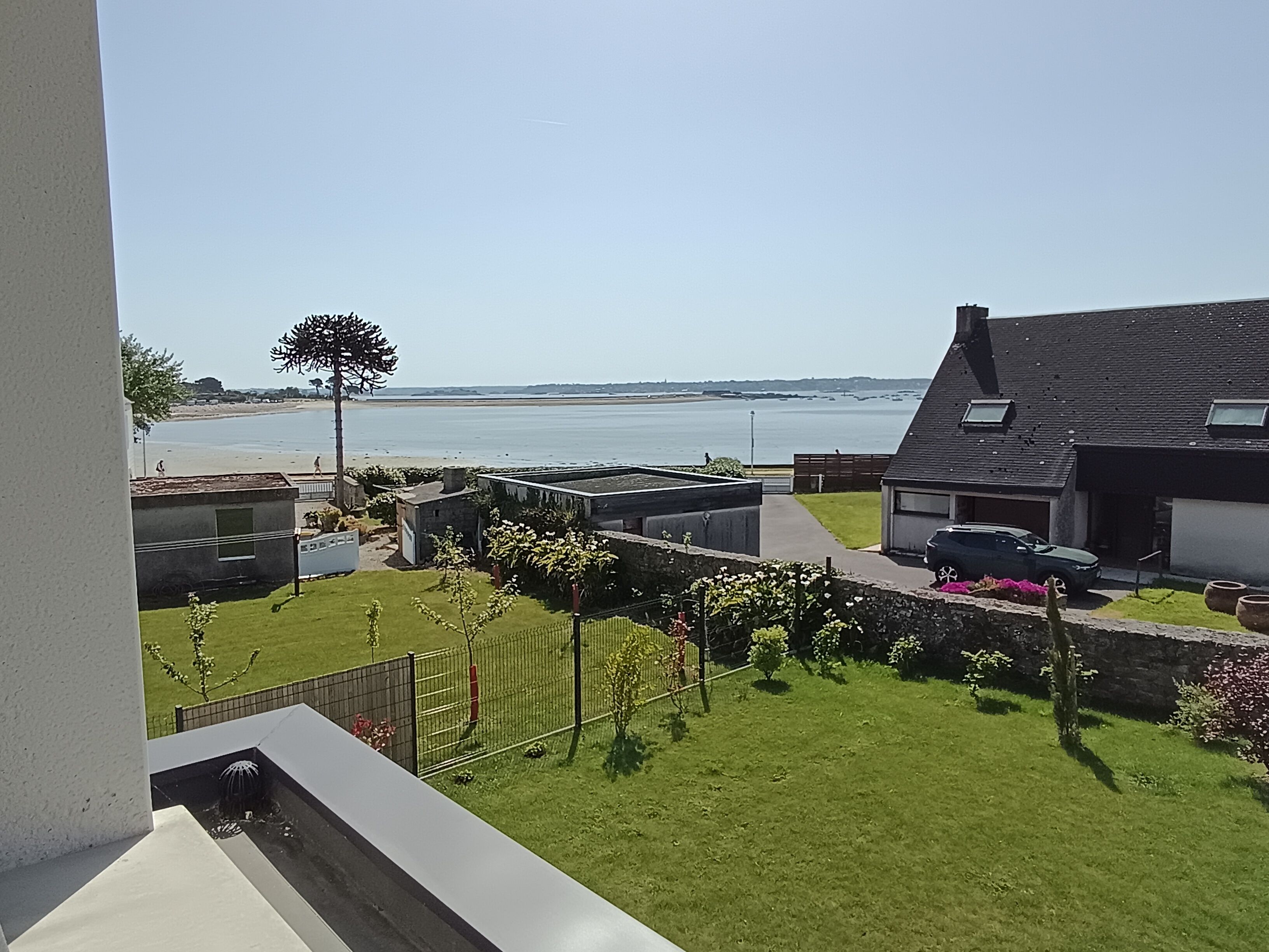 A residential area with a view of the sea, a fenced garden, and a building with a sloped roof.