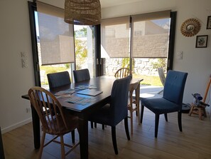 A dining area with a large table, chairs, and a view through the glass doors. - Sea view house 5 minutes walk from the beach and coastal paths. (Saint-Pol-de-Léon)