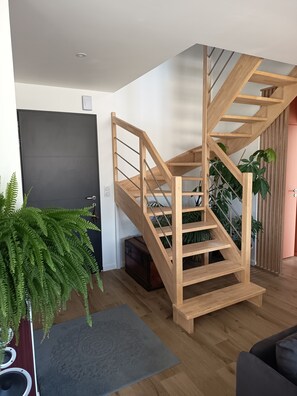 A modern interior with a wooden staircase, a dark door, and a potted fern. - Sea view house 5 minutes walk from the beach and coastal paths. (Saint-Pol-de-Léon)