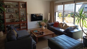 A living room with a flat-screen TV, a bookshelf, a coffee table, and a sofa. - Sea view house 5 minutes walk from the beach and coastal paths. (Saint-Pol-de-Léon)