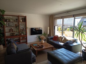 A living room with a flat-screen TV, a bookshelf, a coffee table, and a sofa. - Sea view house 5 minutes walk from the beach and coastal paths. (Saint-Pol-de-Léon)