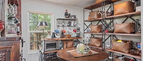 A kitchen with a round wooden table, shelves with baskets, and vintage appliances.