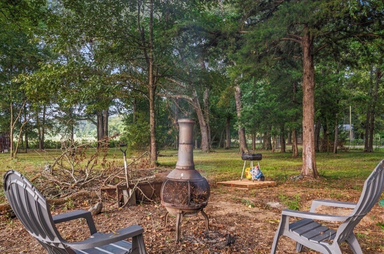 A rustic outdoor setting with a wood-burning stove, two metal chairs, and a small table.