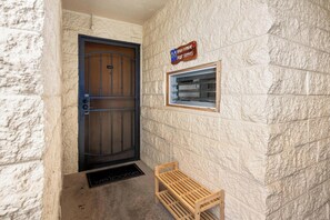 A door with a metal gate, a wooden bench, and a window with a sign above it. - New Listing Keauhou Punahele C202, Ocean Views, Pool (Kailua)