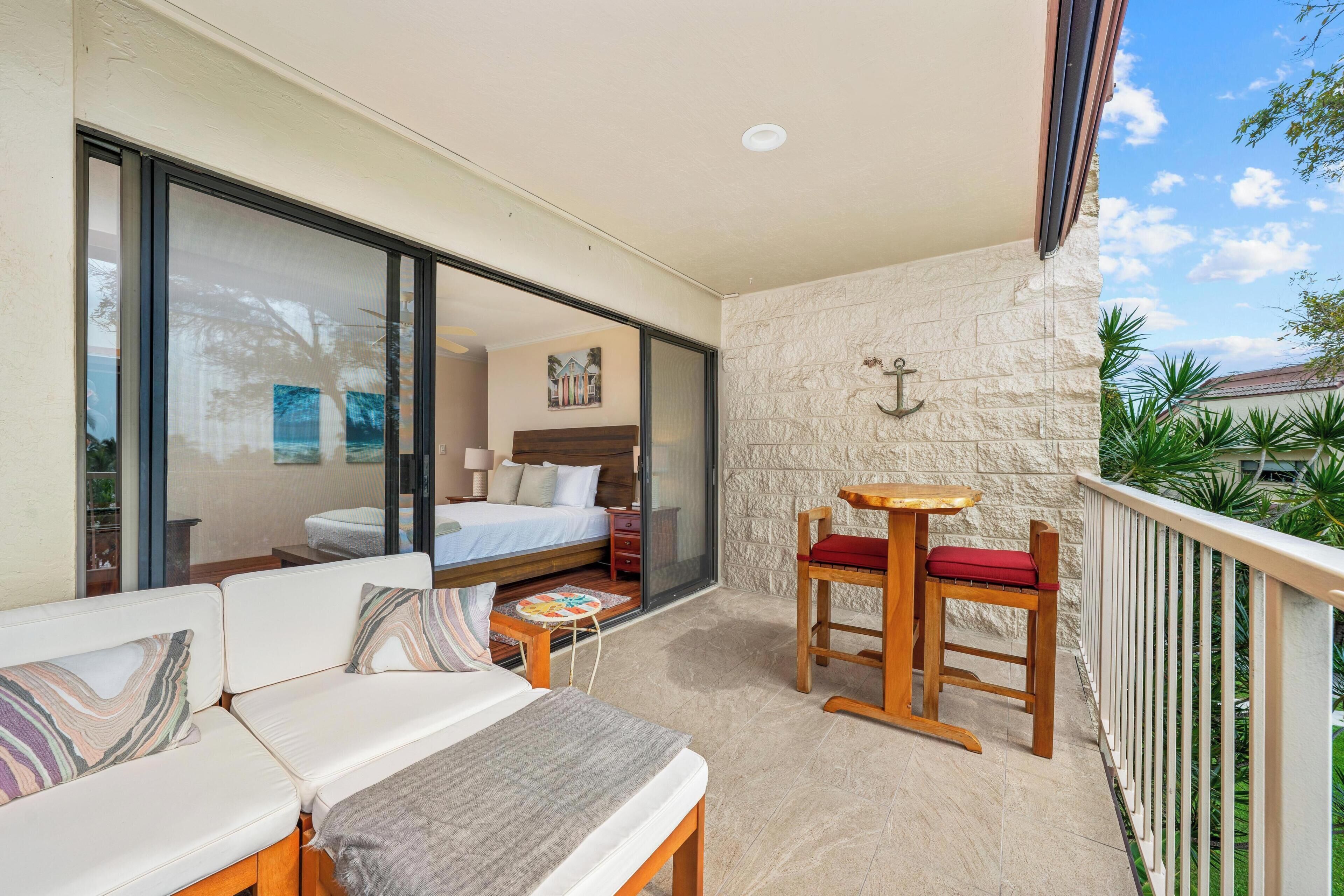 A balcony with a sofa, a small table, and a wooden chair with a cushion.