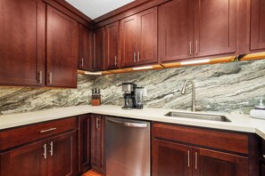 A kitchen with dark wooden cabinets, a marble backsplash, and stainless steel appliances. - New Listing Keauhou Punahele C202, Ocean Views, Pool (Kailua)