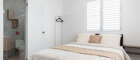 A bedroom with a bed, a window with blinds, a hanging clothes rack, and a toilet.