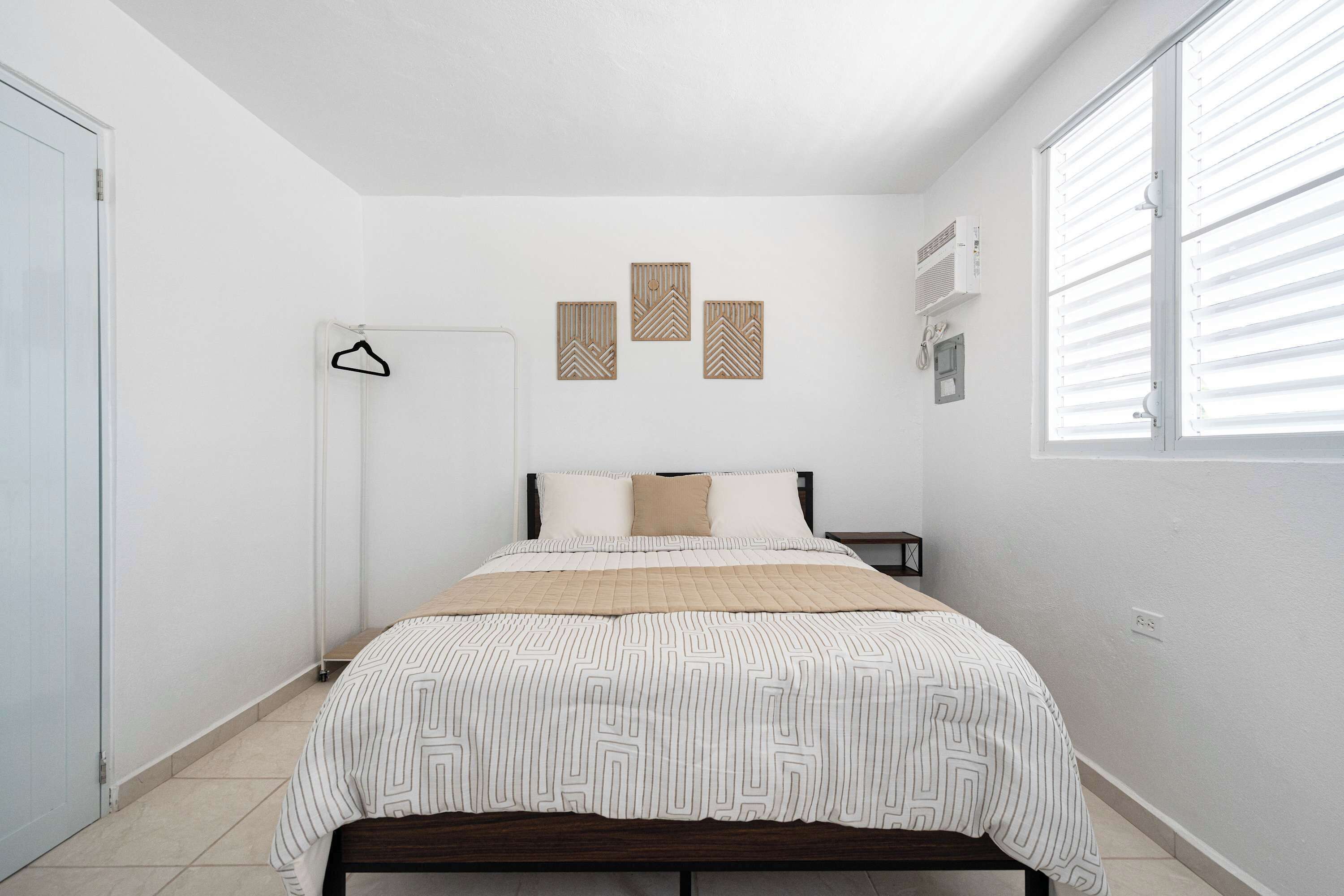 A bedroom with a bed, a bedside table, a hanging light, and a window with blinds.
