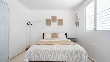 A bedroom with a bed, a bedside table, a hanging light, and a window with blinds.