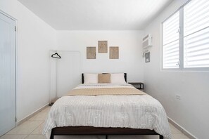 Une chambre à coucher avec un lit, une table de chevet, une lampe suspendue et une fenêtre avec des stores.