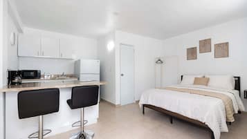 Una habitación compacta con kitchenette, una cama con colcha estampada y una pequeña zona de estar con dos sillas.