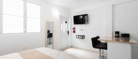 Ein Hotelzimmer mit Bett, Fernseher, Schreibtisch und Stuhl sowie einem Feuerlöscher.