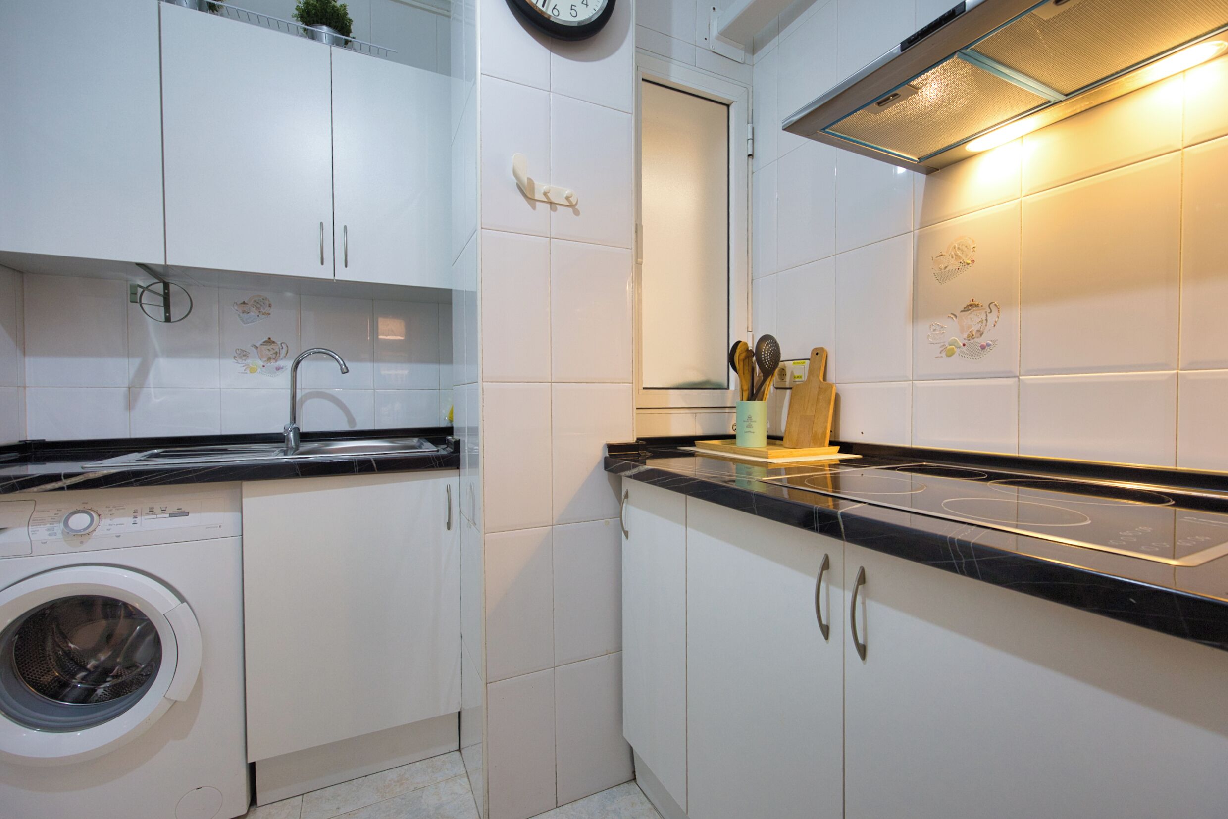 Een keuken met witte kasten, een wasmachine, een spoelbak en een fornuis.