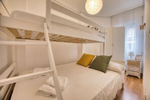 Una cama litera con ropa de cama blanca, una escalera de madera y una pared blanca.