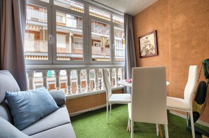 Ein Zimmer mit grünem Kunstgrasanboden, weißen Möbeln, einem Fenster mit Blick auf ein Gebäude mit Balkonen und einem gerahmten Bild an der Wand.