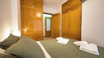 A hotel room with a bed, green bedding, two pillows, a pair of towels, and wooden wardrobes.