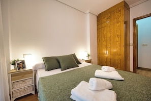 Et hotelværelse med en seng, puder, et natbord med lampe, en træskab og en lyskontakt på væggen.