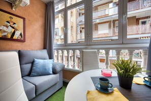 Una sala de estar con un sofá gris, una mesa de centro y vistas a un edificio de apartamentos a través de amplias ventanas.