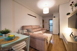 Ein kompakter Wohnbereich mit einer Couch, einem Esstisch mit Stühlen, einer kleinen Küchenzeile und einem an der Wand befestigten Flachbildfernseher.